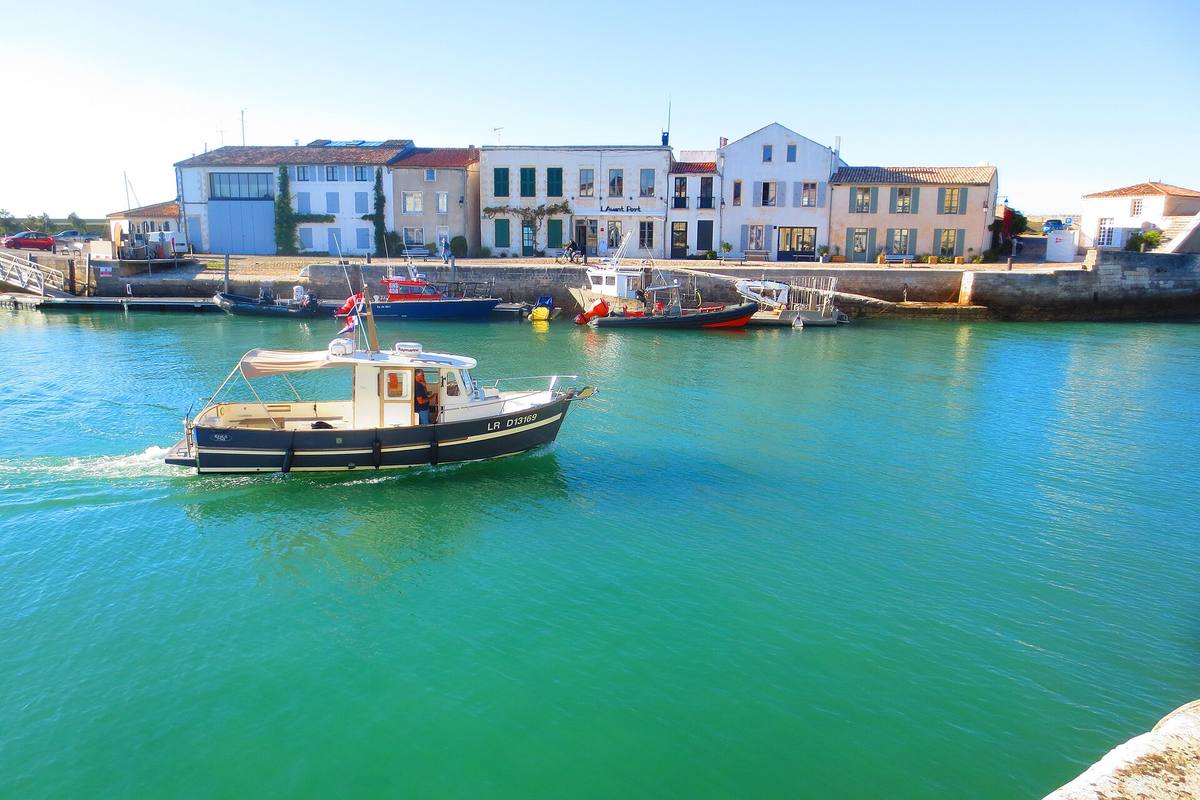 Un bateau de pêche traverse le port de Saint-Martin-de-Ré aux eaux vertes, devant des maisons blanches à volets verts