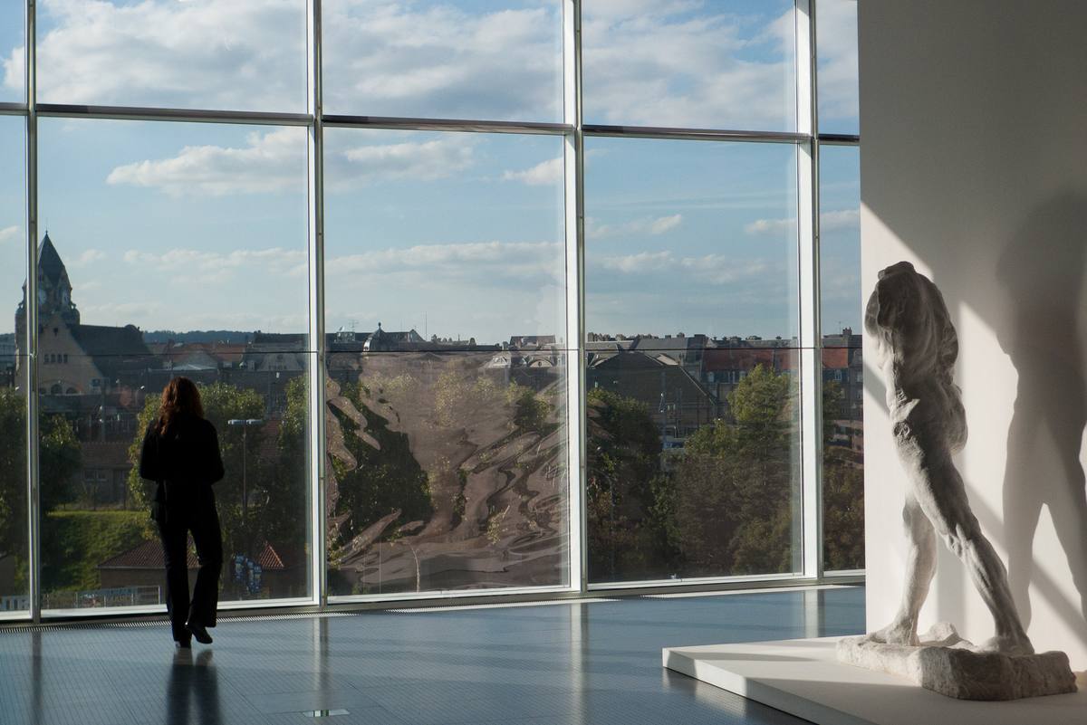 Une galerie du Centre Pompidou-Metz dont la grande baie vitrée donne sur les toits de la ville et le clocher de la gare