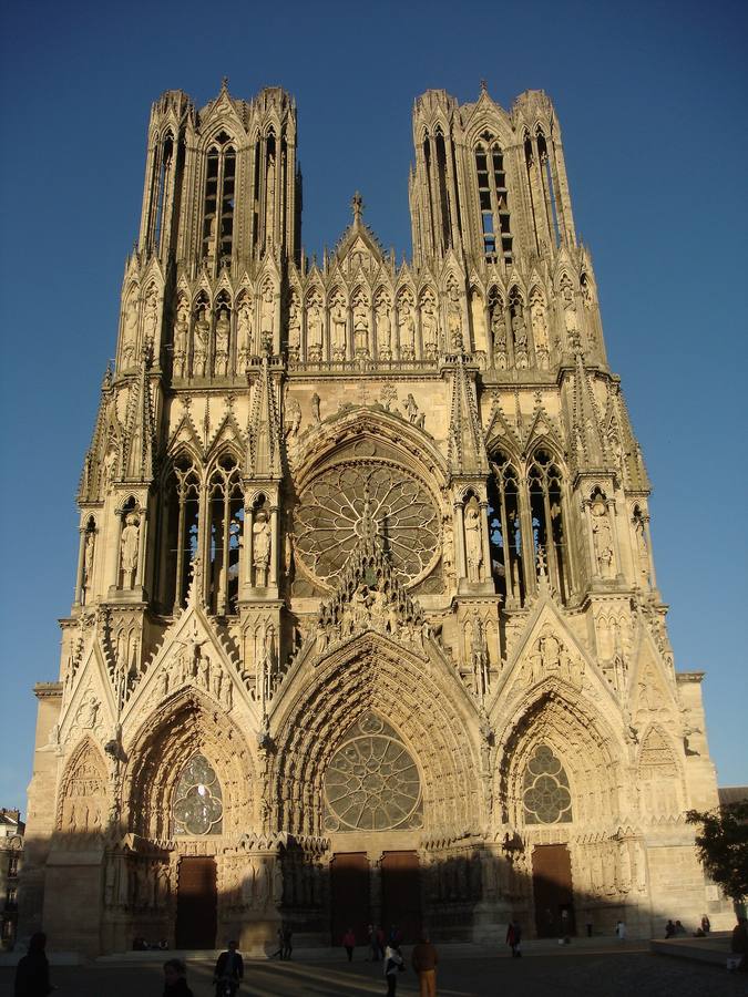 La façade occidentale de la cathédrale Notre-Dame de Reims, éclairée par le soleil couchant sur un ciel bleu
